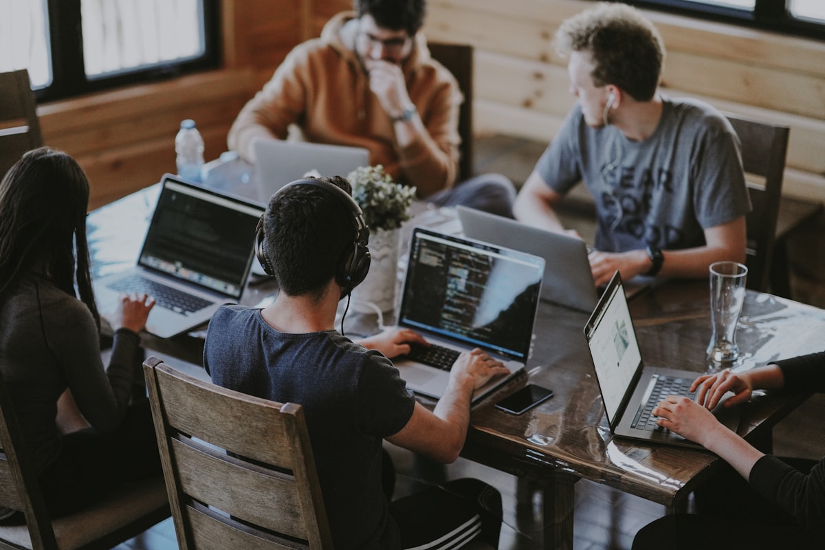 A team building together on laptops around a wooden table